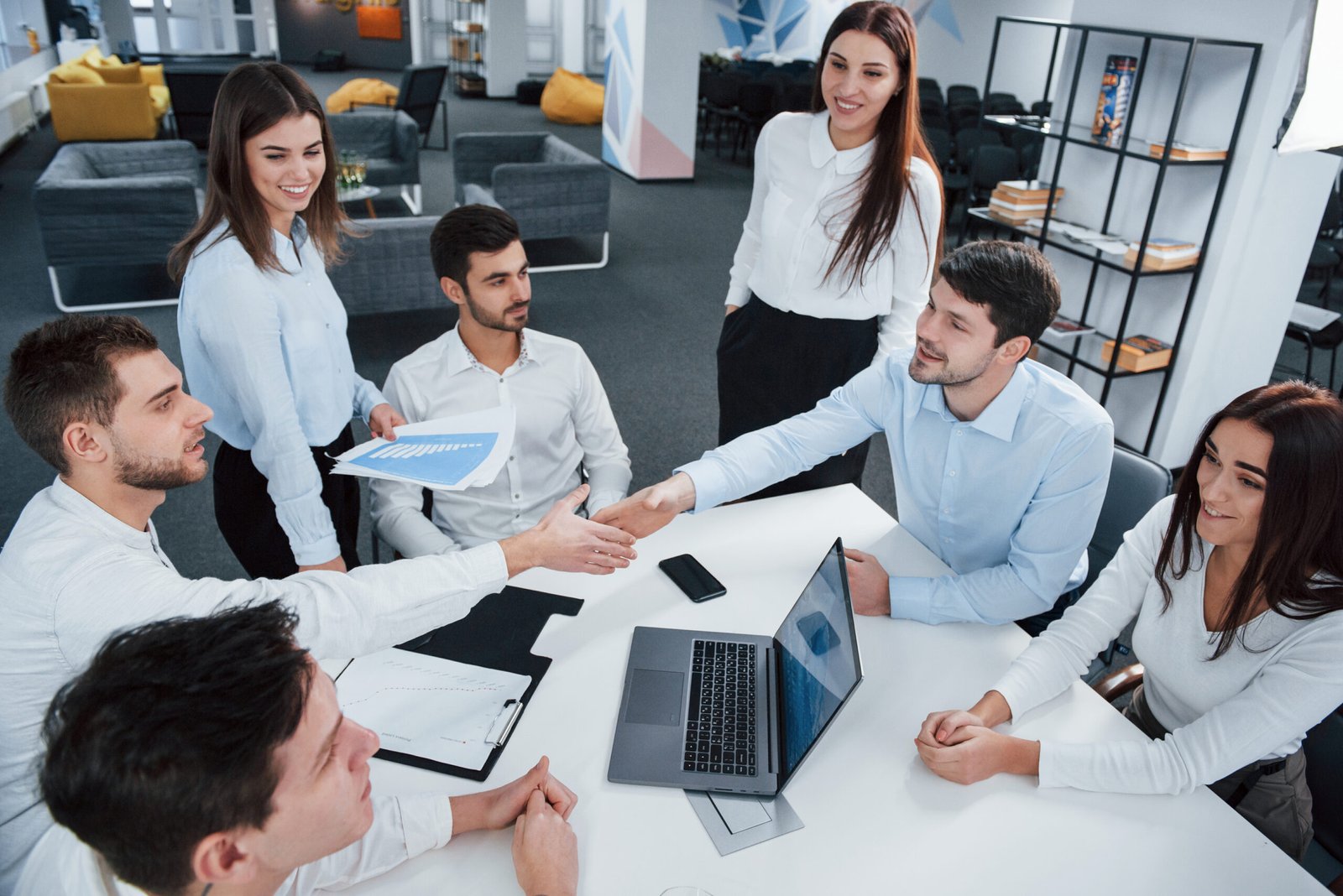 Handshake for success deal. Top view of office workers in classic wear sitting near the table using laptop and documents.